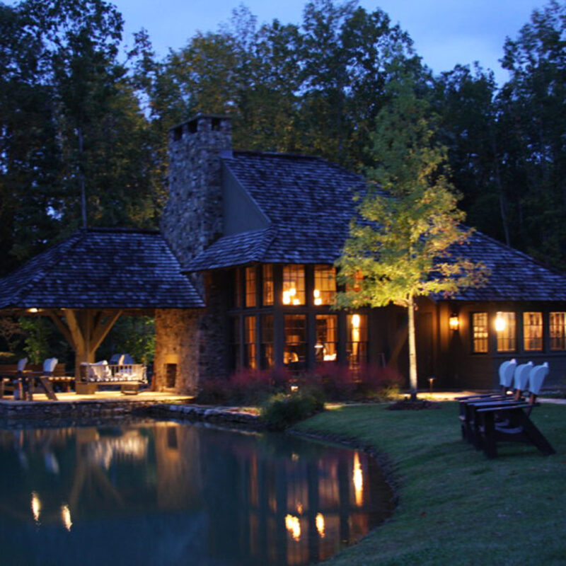 luxury home with landscape lighting reflected by small pond